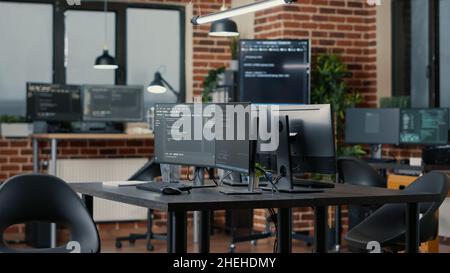 Computer screens running programming code in empty software developing agency office and computers parsing data algorithms in background. Neural network servers cloud computing in data room. Stock Photo