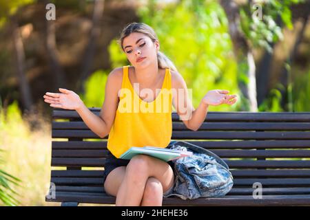 Teenager student girl at outdoors having doubts while raising hands Stock Photo