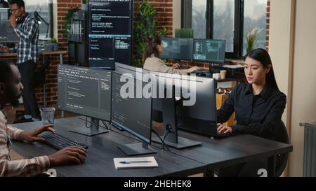 Two focused coders facing each other writing code in software development office while team of coders are developing artificial intelligence. Team of programmers innovating algorithm code. Stock Photo