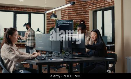 Software engineer typing source code on computer keyboard while colleagues sit down at desk for group project. App developer working in it startup company doing online cloud computing. Stock Photo