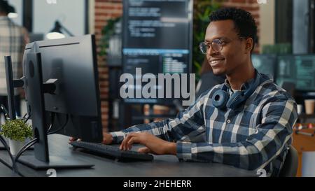 Portrait of software engineer writing code arranging glasses and being happy about parsing results. Smiling programer typing machine learning algorithm on keyboard innovating cyber security. Stock Photo