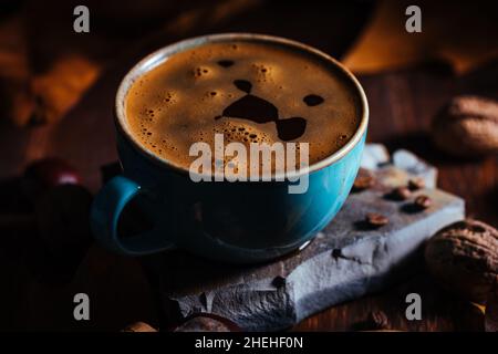 Cup of coffee in blue porcelain cup in a autumn mood with leaves and coffee beans details in setting and background Stock Photo