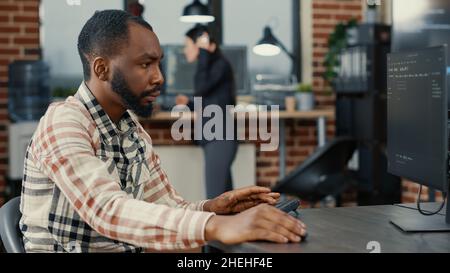Static portrait of african american system engineer working focused looking at computer screen while typing. Software developer in server room writing innovating artificial intelligence algorithm. Stock Photo