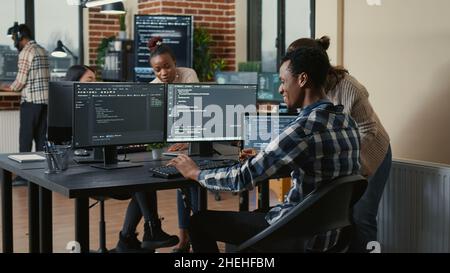Software developer looking at running code on multiple screens takes off glasses and doing high five hand gesture with colleague programer. Programmers celebrating successful online cloud computing. Stock Photo