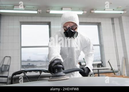 Foreman in protective goggles and suit using car polisher in service Stock Photo