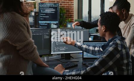 Software developers discussing about source code compiling discovers errors and asks the rest of the team for explanations in front of multiple screens running algorithms. Programmers doing teamwork. Stock Photo