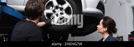 Young workman looking at car wheel near colleague in service, banner Stock Photo