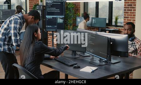 Mixed team of programmers analyzing source code pointing at screens comparing algorithm with user interface on digital tablet. Software developers working on cyber security group project. Stock Photo