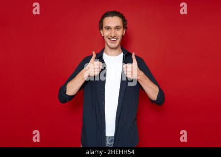 smiling man giving thumbs up sign of approval, quality. casual clothes, isolated on red background Stock Photo