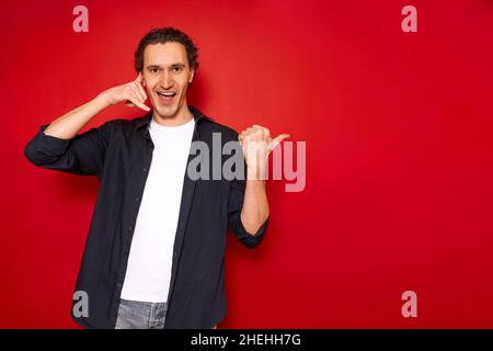 hand sign call me. portrait of young smiling man points with his thumb at vacant empty space Stock Photo