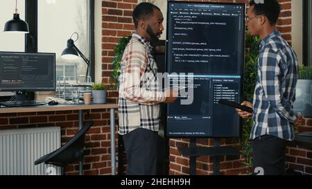 Team of software engineers leaving after analyzing source code on wall screen tv comparing errors using digital tablet. Coders passing coworker programmer writing code for artificial intelligence. Stock Photo