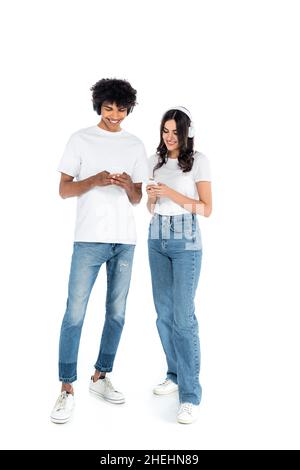 interracial couple in jeans and headphones using mobile phones on white Stock Photo