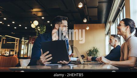 Co-workers smiling at each other while sitting at a table in a co-working space. Two happy businesspeople sharing a workspace in an open office. Cheer Stock Photo