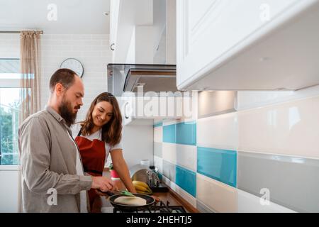 Happy young couple Cooking food on stove and chatting In kitchen interior at cozy home. Family Married couple man and woman during morning routine Stock Photo