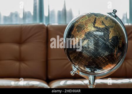 Chiang Rai,Thailand - Sep 06, 2020 : Replica globe on brown leather sofa and white curtains on background. Copy space. No focus, specifically. Stock Photo