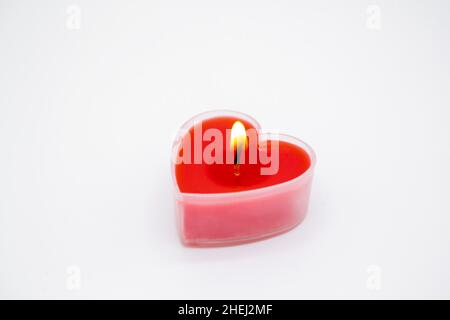 A red heart-shaped candle burns on a white background. Copy space. Concept of love, Valentine's Day, passion. Stock Photo