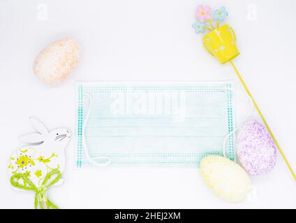 Easter Flat lay with a medical face mask, colorful eggs, decorations in the form of a bucket with a flower and an Easter Bunny. Holiday concept during Stock Photo