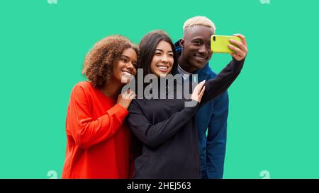 Studio shot of nice young multicultural friends. Beautiful people cheerfully smiling and having fun while making selfie photo. Isolated green backgrou Stock Photo