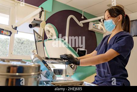 young doctor wearing a mask works on the computer in her dental office Stock Photo
