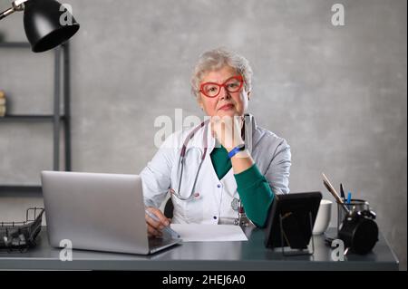 Middle age female doctor using laptop, writing notes with stethoscope on table. Healthcare concept. Medical doctor writing and taking notes Stock Photo