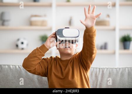 Excited kid using VR glasses, touching something invisible Stock Photo