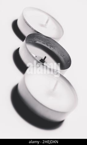 Monochrome white three tea light on white background one after another with one burned Stock Photo