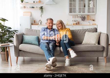 Happy Mature Husband And Wife Using Smartphone Sitting At Home Stock Photo