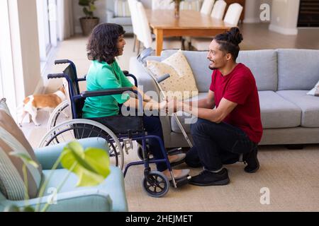 African american man holding hands disabled wife sitting on the wheelchair at home Stock Photo