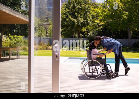 African american disabled woman sitting on wheelchair kissing her husband outdoors Stock Photo