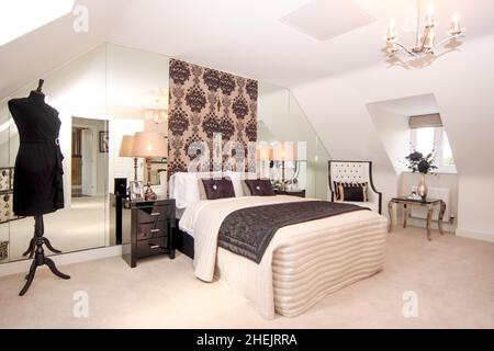Cream and black bedroom in modern new build house,double kingsize bed,chair,dormer window,attic room,bedside lighting, mirror wall. Stock Photo
