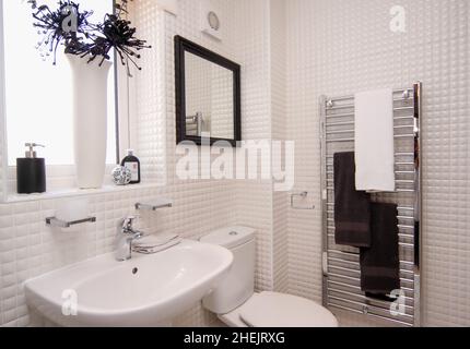 Bathroom sink,toilet and towel rail with small white tiled walls in modern new build house. Stock Photo