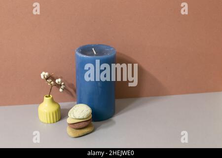 Navy candle and stack of pebble stones and dry plant on gray table. brown wall background. home decor interior Stock Photo