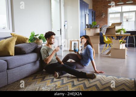 Happy young biracial couple talking while taking coffee break from relocating new home Stock Photo