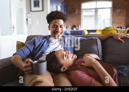 Cheerful young biracial couple talking while relaxing on sofa at home Stock Photo