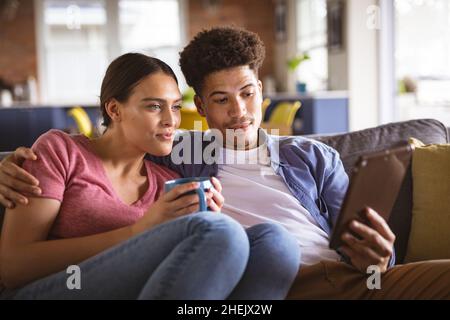 Young biracial couple watching video together on digital tablet sitting on sofa at home Stock Photo
