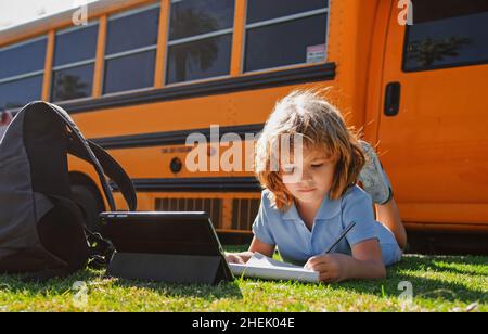 Smart schoolboy on laying on grass with digital tablet at school park. Child using gadgets to study outdoor. Education and learning for kids. Stock Photo