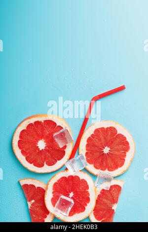A composition of grapefruit slices and ice cubes with a straw on a blue background in the form of a refreshing drink. Top view, free space Stock Photo