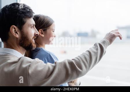 happy father pointing at window near smiling daughter in airport Stock Photo