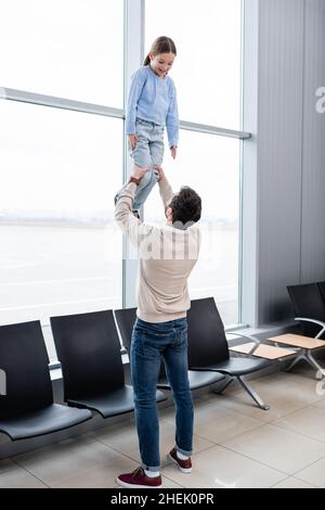 father lifting happy daughter in airport lounge Stock Photo