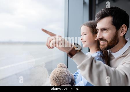 happy father pointing with finger at window near cheerful daughter in airport Stock Photo