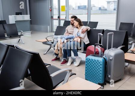girl sleeping on knees of tired parents in airport lounge Stock Photo