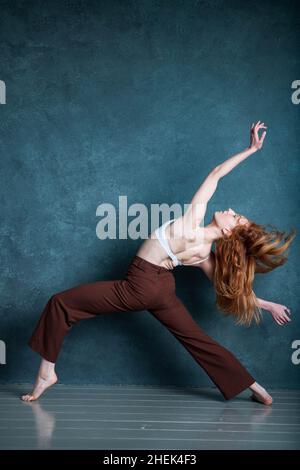 Petitie dancer with red auburn hair dancing against grey backdrop Stock Photo