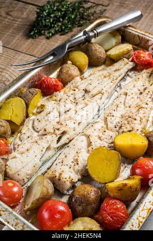 Hake fish fillet, roasted fish meat with tomato and potato. Wooden background. Top view Stock Photo