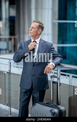 Serene elegant businessperson with the trolley suitcase looking away Stock Photo