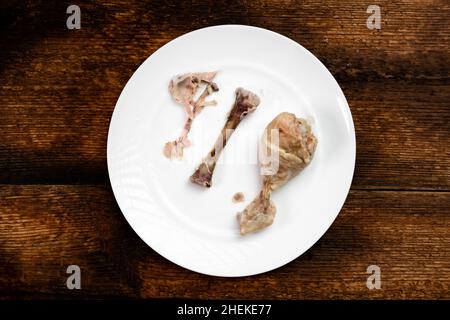 Two boiled half-eaten chicken legs on a white plate. Dark wooden background. Diet food. Stock Photo