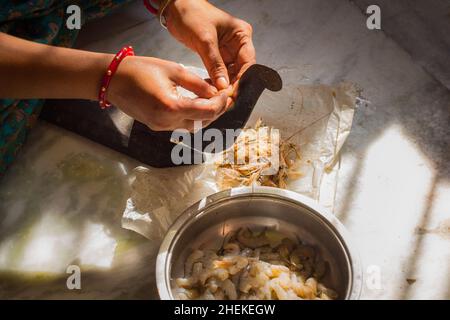indian woman cutting or dressing raw shrimp for cooking in desi cutter or boti. hands wearing traditional bangle. natural light shot in kitchen floor. Stock Photo