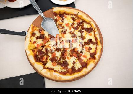 Thin crust homemade pizza with bacon, ham and cheese on a wooden tray Stock Photo