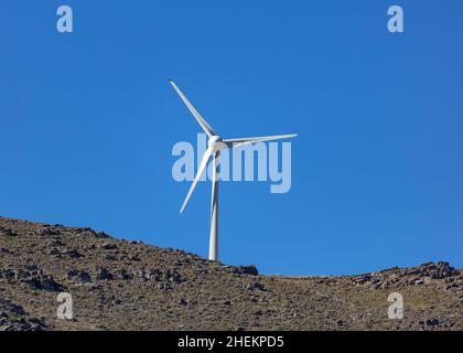 Renewable power energy, Wind turbine, electric generator on a rocky hill, clear blue sky background, sunny day. Stock Photo