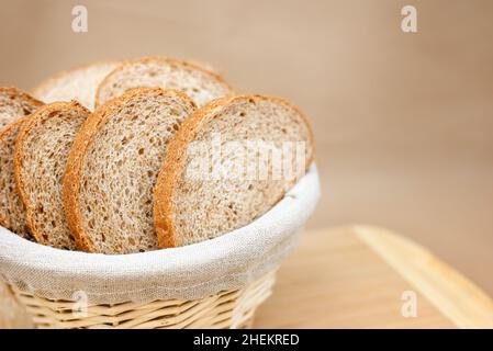 Fresh cereal bread in a wicker basket. The bread is sliced. Beige background, wooden board, linen cloth in a basket. Free space for text. Stock Photo