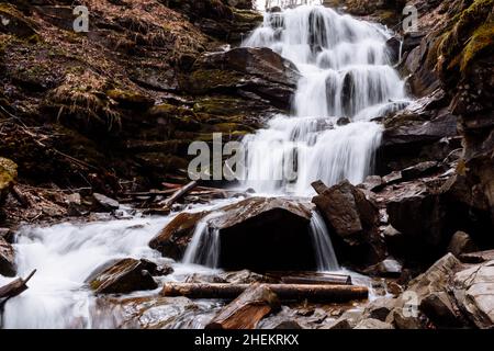 Cascading down a small mountain stream, the water runs over basalt boulders. A small waterfall runs through the moss
